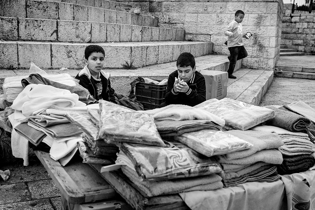 Two young people behind piles of clothing on steps.